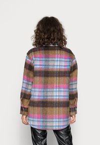Camisa de franela a cuadros en marrón, azul y rosa, con mangas largas, puños con botones y un dobladillo curvado. Textura suave, ajuste relajado.