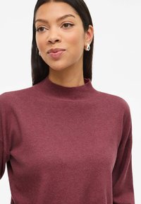 Bordeaux hooghalstrui gemaakt van ribgebreide stof; heeft een ontspannen pasvorm en lange mouwen. Textuur, zachte uitstraling met minimale details.
