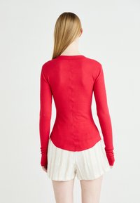 Κόκκινη, ριγωτή μπλούζα με μακριά μανίκια και εφαρμοστή σχεδίαση, στρογγυλή βάση και επιμήκεις καρπούς, συνδυασμένη με ελαφριά, ριγέ σορτς.