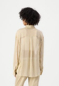 Ľahká, priesvitná béžová blúzka s vertikálnymi bordovými pruhmi, dlhými rukávmi a špicatým golierom, s voľným strihom a zapínaním na gombíky na manžetách.