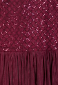 Vinröd klänning med ett paljettbesatt diamantmönster på en texturerad överdel och en veckad nederdel, tillverkad av ett lätt och mjukt tyg.