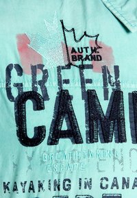 Türkiz színű vászon ing, fekete hímezett "GREEN CAMP" szöveggel és juharlevél díszítéssel. Puha tapintású, képernyőnyomott részletekkel.