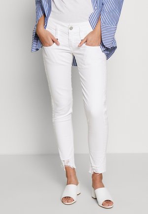 Vita smala jeans med fransade kanter, som har en klassisk femfickdesign och knäppning. Parat med vita öppna tår-tovallar.