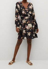 Vestido floral tipo wrap con mangas largas, escote en forma de V, fondo negro y diversos patrones de flores en tonos pastel; cuenta con una cintura ajustada y una falda acampanada.