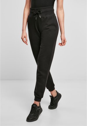 Czarne spodnie dresowe z prążkowanym pasem i mankietami, noszone z czarnymi tenisówkami i czarnym topem bez rękawów, stojące na jednolitym tle.