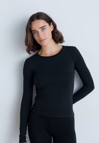 Top fitted a maniche lunghe nero realizzato in un tessuto morbido e elasticizzato. Presenta un collo rotondo e una texture liscia senza cuciture visibili.