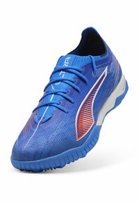 Niebieski but sportowy z teksturowaną cholewką, z gradientowym wzorem, kontrastującymi pomarańczowymi akcentami i białą podeszwą dla lepszej przyczepności.