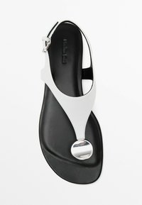 Hvide sandaler med en sort sål, der har en glat læderoverdel, åben tå og en rund metallisk detalje for ekstra flair.