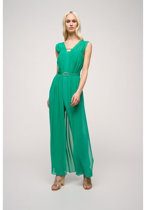 Groene, mouwloze jumpsuit van lichtgewicht stof, met plooien, een tailleband met een vierkante gesp en een wijdbenige uitstraling. Gouden haksandalen.