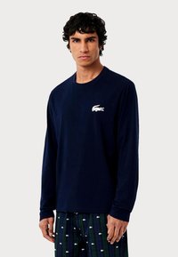 Námořnická modrá dámská tričko s dlouhým rukávem z bavlny, s kulatým výstřihem a bílým vyšívaným logem krokodýla na levém prsu.