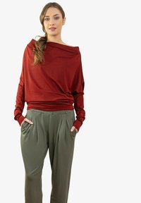 Czerwona bluzka z długim rękawem o luźnym kroju i luźnym dekoltem, zestawiona z oliwkowozielonymi plisowanymi spodniami z bocznymi kieszeniami. Miękka faktura materiału.