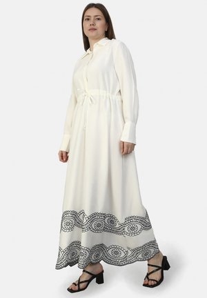 Lange witte jurk van lichtgewicht stof, met een trekkoord in de taille, lange mouwen en zwarte bloemenborduursels langs de zoom.