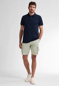 Námořnická polokošile s malými zelenými a žlutými vzory, kombinovaná s lehkými nákladními šortkami a bílými teniskami. Lehká látka, klasický střih.