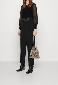 Svart långärmad topp med genomskinliga puffärmar, svarta byxor, ankelhöga svarta klackstövlar och en handväska med leopardmönster och dragsnöre.