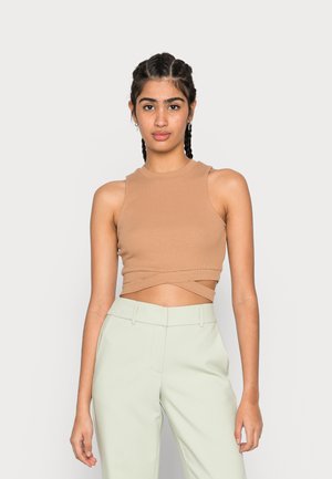 Top crop canelado bege com gola alta e bainha cruzada, combinado com calças de alfaiataria verde-claro. Textura suave, design ajustado.
