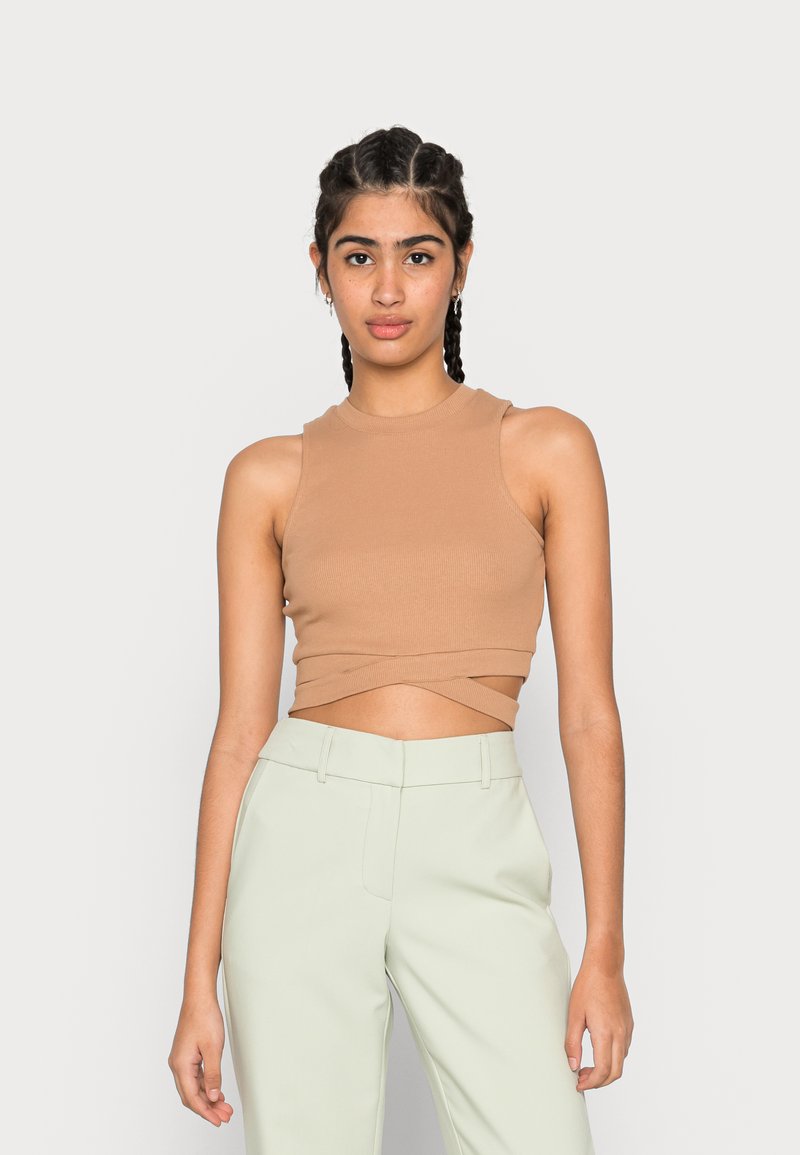 Top crop canelado bege com gola alta e bainha cruzada, combinado com calças de alfaiataria verde-claro. Textura suave, design ajustado.