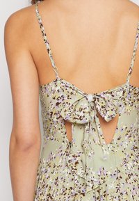 Grün-blaues Kleid mit floralen Mustern, dünnen Trägern, einem gebundenen Rückendetail und einem offenen Ausschnitt. Leichter Stoff mit weicher Textur.