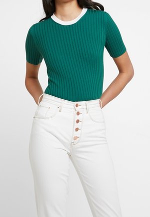 Groen geribbelde top met korte mouwen en witte ronde halslijn, gecombineerd met hoge witte jeans met een knopen-front.