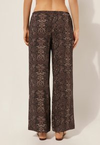 Pantalones amplios de estampado de serpiente marrón con una textura suave y cintura elástica. El dobladillo es recto y llega hasta los tobillos.