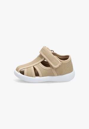 Sandalia beige para niño pequeño con tira de velcro ajustable y suela de goma blanca, con punta abierta y diseño de tela transpirable.