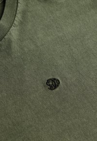 Olivengrøn bomulds-t-shirt med rund halsudskæring, med en broderet logo på venstre side. Glat tekstur og medium tykkelse.