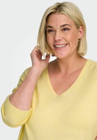 Pull jaune en maille douce avec un col en V et une coupe décontractée. Manches longues avec poignets côtelés. Tissu léger et texturé.