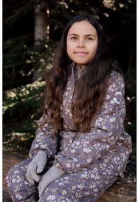 Mono acolchado con estampado floral púrpura, cuello alto y puños elásticos, combinado con guantes gris claro, sobre un fondo natural.