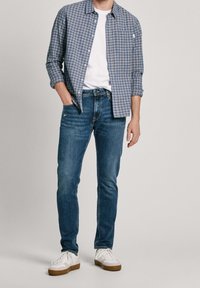 Camisa de cuadro azul sobre una camiseta blanca, combinada con jeans azul oscuro y zapatillas blancas con detalles en marrón.