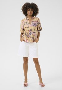Camicia a maniche corte con colletto in colori pastello e motivi astratti; abbinata a pantaloncini di jeans bianchi e sandali con tacco rosa.