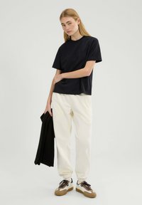 Czarny t-shirt z krótkim rękawem o luźnym kroju, zestawiony z kremowymi spodniami dresowymi i brązowymi sneakersami. Prosty design bez widocznych wzorów.