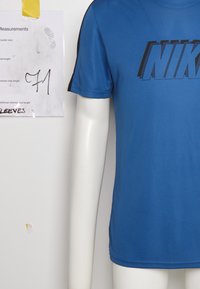 Camisa de manga corta azul de Nike, hecha de una tela suave, con un audaz logo negro en el pecho y acentos negros en los hombros.
