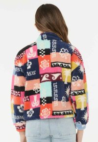 Mønstret fleecejakke i flere farver med et patchwork-design indeholdende geometriske og blomsteragtige mønstre i nuancer af pink, blå, orange og sort.