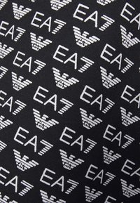 Czarna tkanina z powtarzającym się wzorem białych logo z literami "EA7" oraz stylizowanymi skrzydłami. Gładka tekstura.