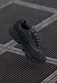 Black athletic shoe with mesh and synthetic materials. Features a rounded toe, cushioned sole, and prominent "N" logo on the side.