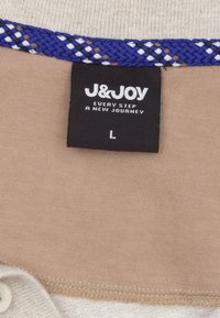 Beige stof met een gestructureerd bovenste gedeelte en een gladde onderste sectie, met een blauwe geweven accent en een zwart label met witte tekst.