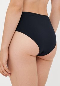 Woman wearing high-waisted black underwear, showing lower back and upper thigh against a plain white background.