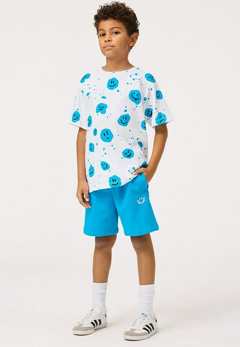 Vit t-shirt med blåa leende ansiktstryck, ihop med enfärgade blå shorts. Ovanför plagget har en avslappnad passform och är tillverkat av lättviktig tyg.
