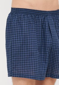 Σκούρο μπλε καρό μποξεράκια με ελαστική μέση. Το υλικό είναι ελαφρύ ύφασμα, με μικρούς τετραγώνους σε σκούρους και ανοιχτούς τόνους.