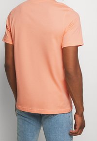 Kortärmad T-shirt med rund hals i mjuk persikofärgad bomull. Har sydda ärmar och rak fåll. Bärs med ljusblå jeans.