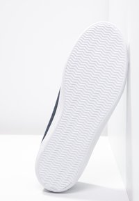 Baskets en tissu bleu marine avec une semelle en caoutchouc blanc, présentant un motif en zigzag texturé pour l'adhérence et un design épuré à profil bas.