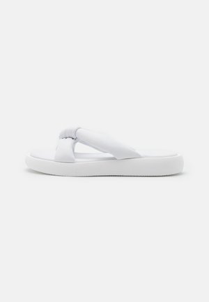 Sandalia de goma blanca con correas de tela anudadas, suela plana y superficie lisa. Diseño simple y construcción ligera.