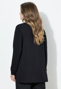 Schwarzes Langarmshirt aus weichem Stoff mit lockerem Schnitt, abgerundetem Saum und schlichtem Design, getragen zu dunkler Jeanshose.