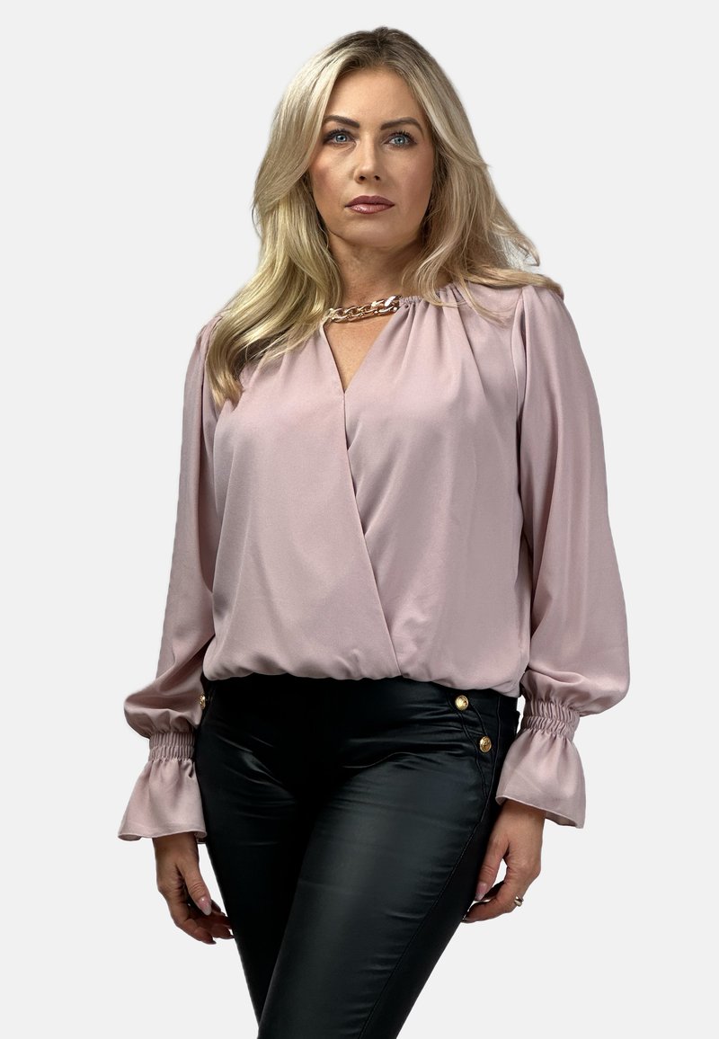 Blador różowa bluzka o kroju kopertowym, z długimi rękawami z falbanami przy mankietach i złotym łańcuszkiem przy dekolcie. Połączona z czarnymi spodniami.
