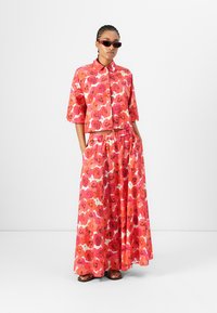 Zweiteiliges Outfit mit einem Kurzarm-Hemd mit Kragen und einem langen, fließenden Rock. Beide Teile sind mit leuchtend roten und pinken Blumen gemustert.
