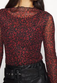 Röd genomskinlig långärmad topp med ett svart leopardmönster, med en lätt volang i halsringningen och matchad med högmidjade svarta läderbyxor.