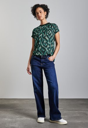Groen en teal gestreept t-shirt met korte mouwen, gecombineerd met donkerblauwe wijde jeans en witte sneakers. Natuurlijke haardracht en een casual houding.