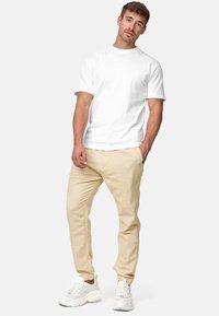 Camiseta de algodón blanca de manga corta, combinada con pantalones beige con un patrón texturizado, complementados con zapatillas blancas.