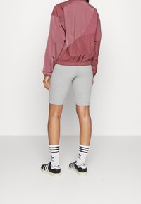 Vínová větrovka s texturovaným vzorem, doplněná o šedé legíny a černo-bílé pruhované ponožky, nošené s černou obuví.