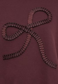 Tecido bordeaux com um design de laço texturizado feito de fita, apresentando detalhes pregueados ao longo das bordas para um toque adicional.