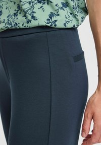 Navy stretch fabric pants with a smooth texture, featuring a small pocket detail on the side and a fitted design along the leg.